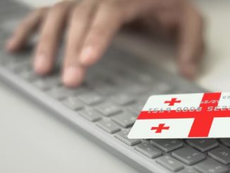 Пожилой человек в Грузии держит банковскую карту и телефон, на фоне логотипа Национального банка Грузии.