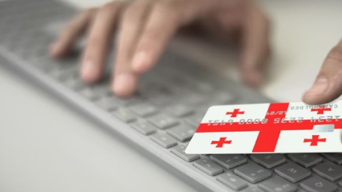 Пожилой человек в Грузии держит банковскую карту и телефон, на фоне логотипа Национального банка Грузии. Пожилой человек в Грузии держит банковскую карту и телефон, на фоне логотипа Национального банка Грузии.